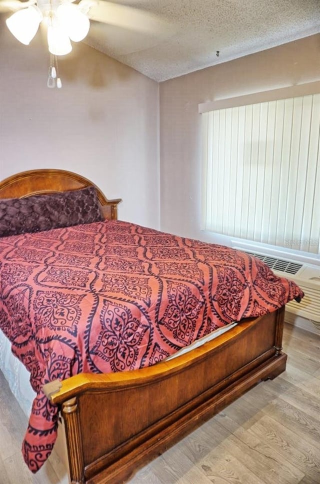 bedroom with ceiling fan, wood finished floors, and a textured ceiling