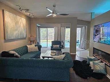 living area featuring ceiling fan and a glass covered fireplace