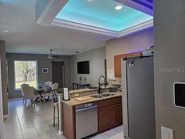 kitchen with a peninsula, stainless steel appliances, stone counters, a kitchen bar, and a sink