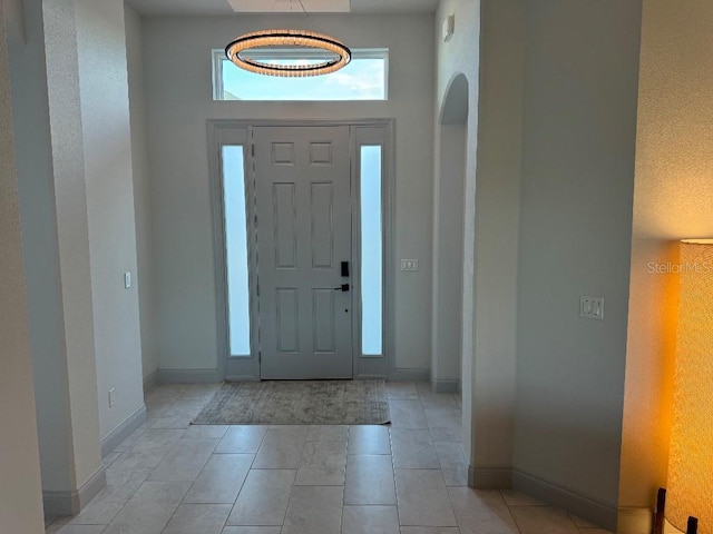 foyer featuring light tile patterned floors, arched walkways, and baseboards