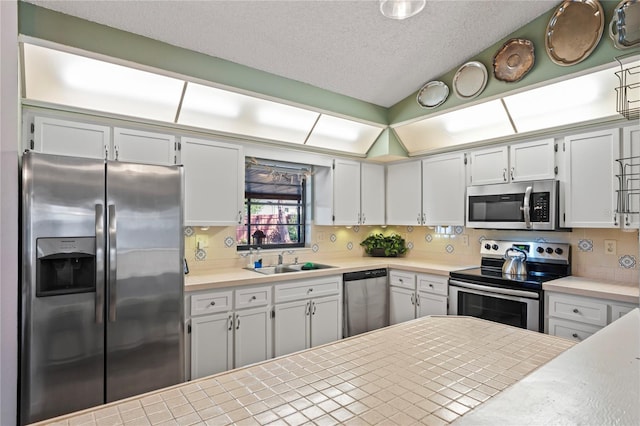 kitchen featuring stainless steel appliances, vaulted ceiling, a sink, and decorative backsplash