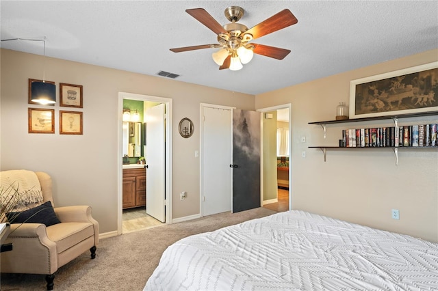 bedroom with light colored carpet, visible vents, ensuite bathroom, a textured ceiling, and baseboards