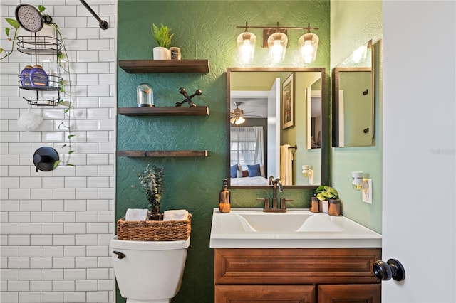 bathroom featuring a textured wall, vanity, toilet, and ceiling fan