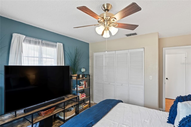 bedroom with a textured ceiling, a closet, visible vents, and a ceiling fan