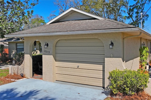 exterior space with a garage, stucco siding, and roof with shingles