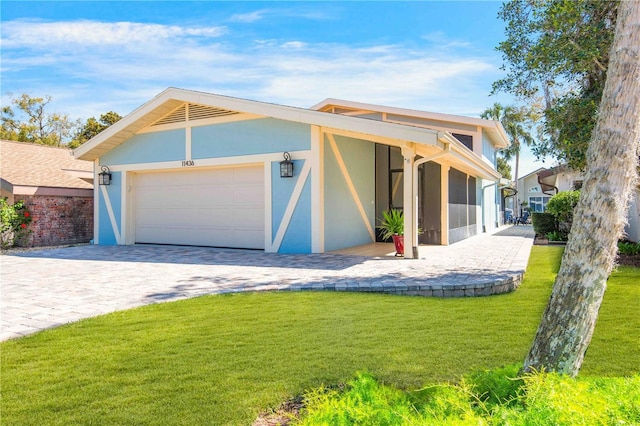 view of front of house featuring stucco siding, a sunroom, a front yard, decorative driveway, and an attached garage