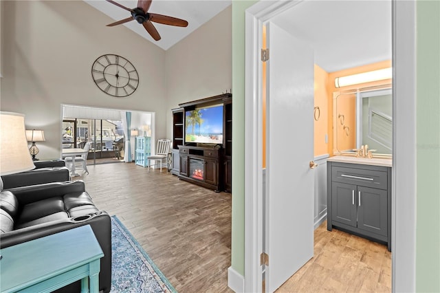 living area featuring light wood-style floors, ceiling fan, and high vaulted ceiling