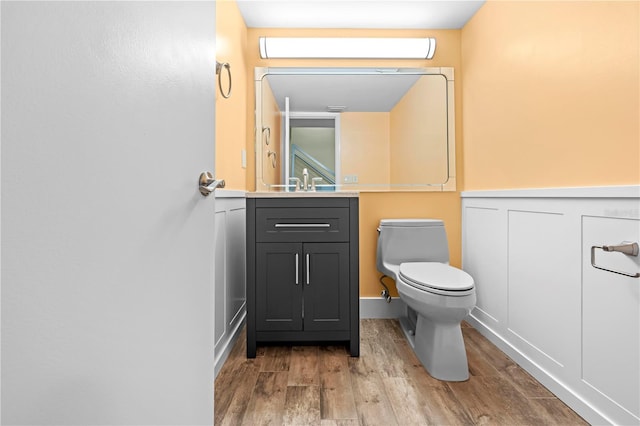 bathroom featuring a wainscoted wall, a decorative wall, toilet, vanity, and wood finished floors