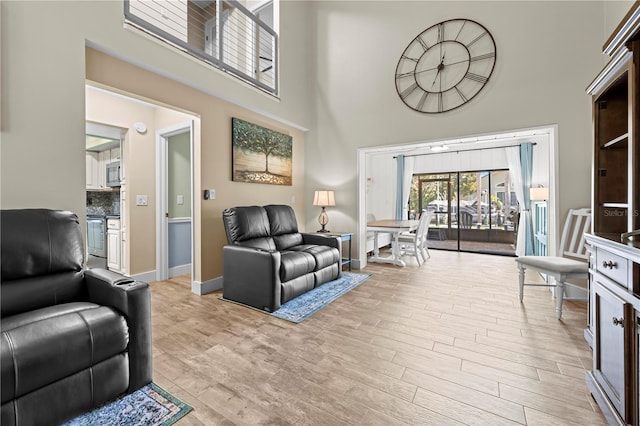 living room with baseboards, a high ceiling, and light wood-style floors