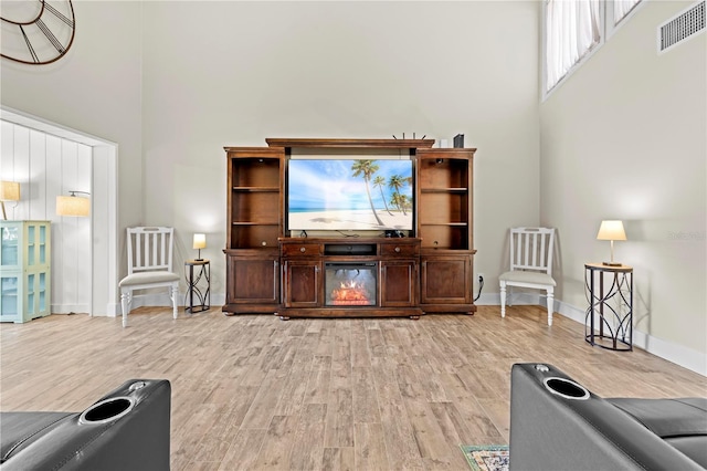 living area featuring light wood-type flooring, visible vents, and a high ceiling