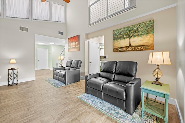 living area featuring a towering ceiling, baseboards, visible vents, and wood finished floors