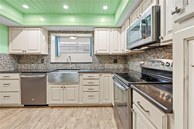 kitchen featuring stainless steel appliances, tasteful backsplash, dark countertops, and light wood-style floors