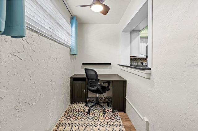 office featuring a ceiling fan, wood finished floors, and a textured wall