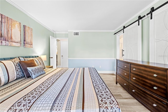 bedroom with a barn door, visible vents, baseboards, light wood-style flooring, and ornamental molding