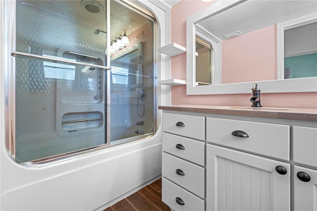 full bath featuring visible vents, combined bath / shower with glass door, vanity, a textured ceiling, and wood finished floors