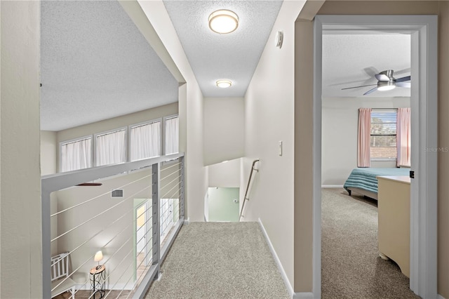 corridor with a textured ceiling, carpet flooring, an upstairs landing, and baseboards