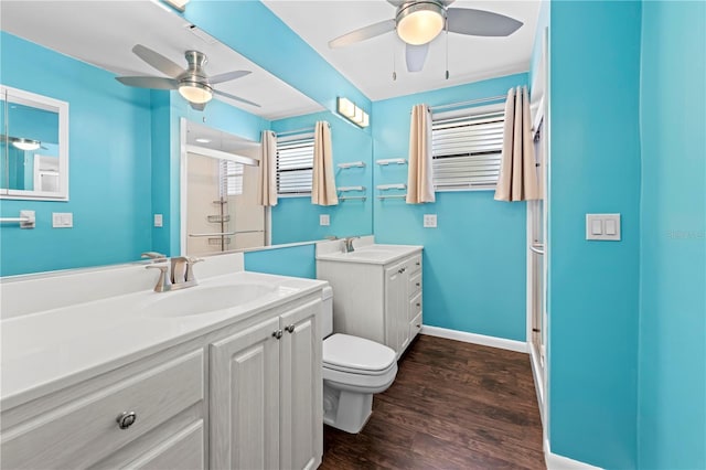 bathroom with a stall shower, toilet, wood finished floors, a sink, and two vanities