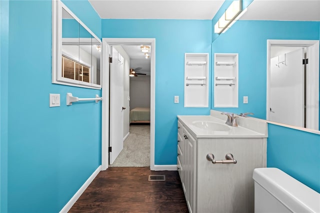 half bath with toilet, wood finished floors, vanity, visible vents, and baseboards