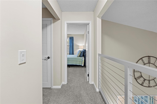 corridor featuring carpet floors, an upstairs landing, a textured ceiling, and baseboards