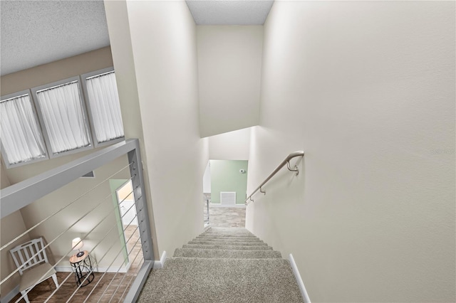 staircase featuring a high ceiling, carpet flooring, a textured ceiling, and baseboards