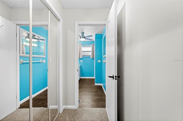 hallway with carpet flooring, a textured ceiling, and baseboards