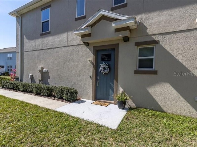 view of exterior entry featuring a lawn and stucco siding