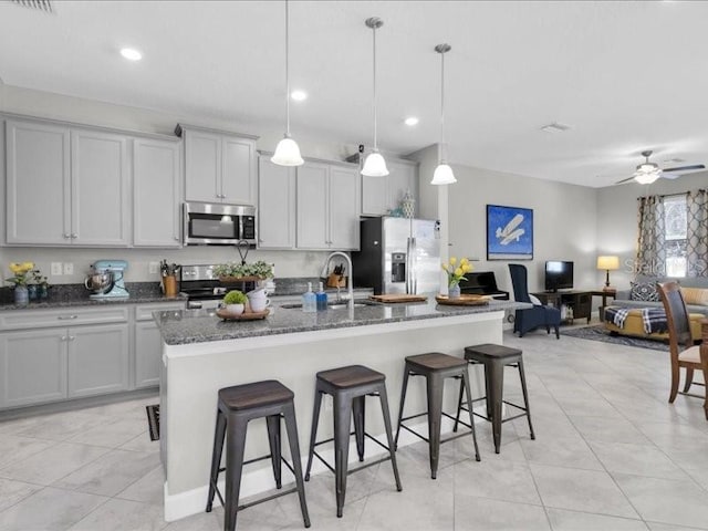 kitchen with a ceiling fan, an island with sink, a breakfast bar, dark stone countertops, and stainless steel appliances