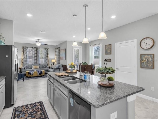 kitchen with decorative light fixtures, stainless steel appliances, a kitchen island with sink, a sink, and dark stone counters