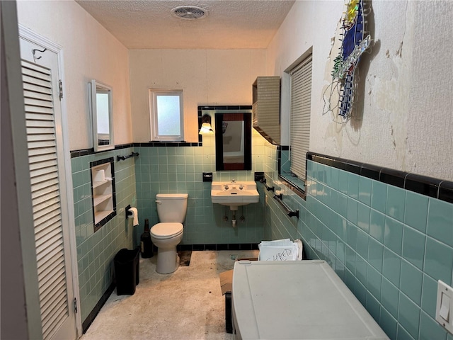 bathroom with visible vents, toilet, a sink, a textured ceiling, and tile walls