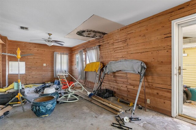 interior space with ceiling fan, wooden walls, and visible vents