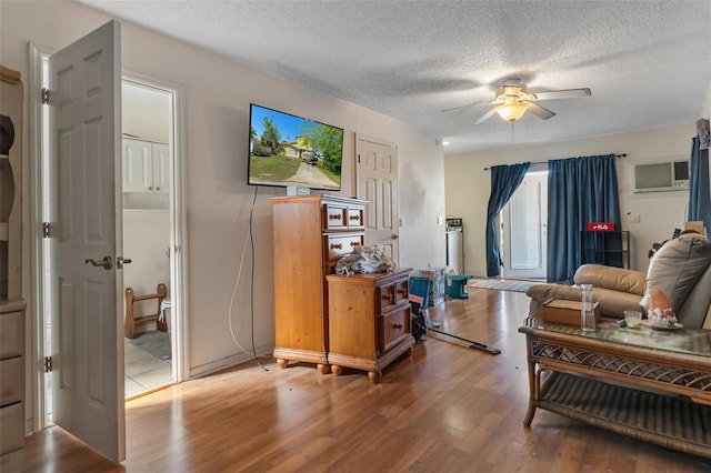 living area featuring a wall mounted AC, ceiling fan, a textured ceiling, and wood finished floors