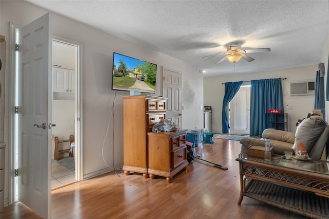 living area with a textured ceiling, an AC wall unit, wood finished floors, and a ceiling fan