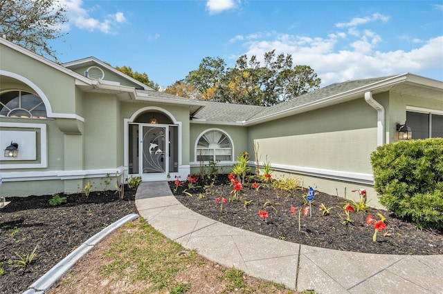 view of exterior entry with roof with shingles, an attached garage, and stucco siding