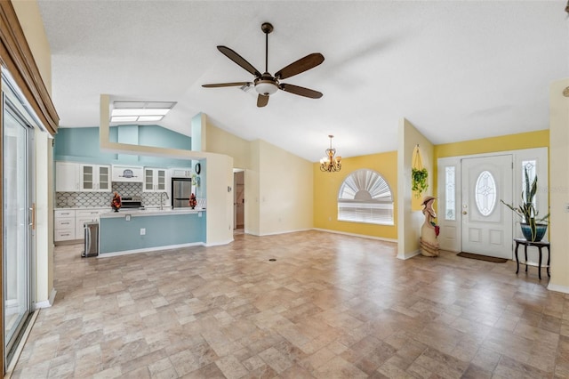 unfurnished living room with baseboards, stone finish flooring, vaulted ceiling, a sink, and ceiling fan with notable chandelier