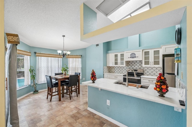 kitchen featuring stainless steel appliances, a peninsula, white cabinets, tasteful backsplash, and glass insert cabinets