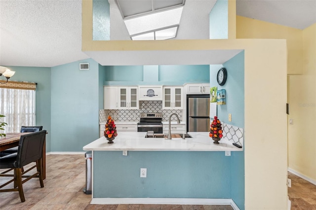 kitchen featuring appliances with stainless steel finishes, a peninsula, vaulted ceiling, white cabinetry, and a sink