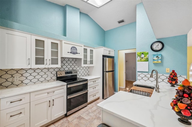 kitchen featuring stainless steel appliances, lofted ceiling, white cabinetry, a sink, and light stone countertops