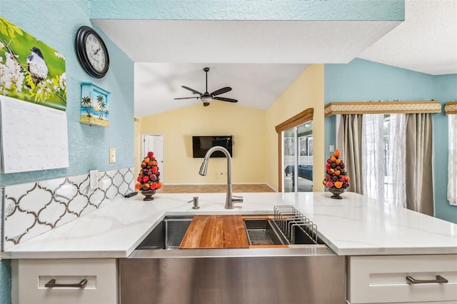 kitchen with open floor plan, vaulted ceiling, a ceiling fan, and light stone countertops