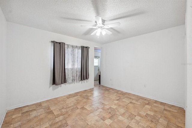 empty room featuring ceiling fan, stone finish floor, a textured ceiling, and baseboards