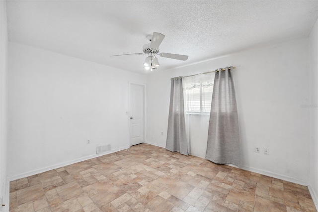 empty room with a textured ceiling, ceiling fan, visible vents, baseboards, and stone finish flooring