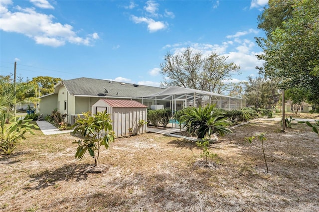 back of house with an outbuilding, glass enclosure, an outdoor pool, a shed, and stucco siding