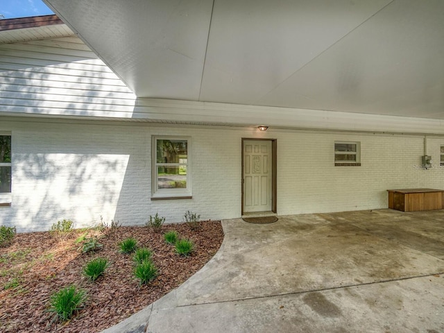 view of exterior entry featuring an attached carport and brick siding