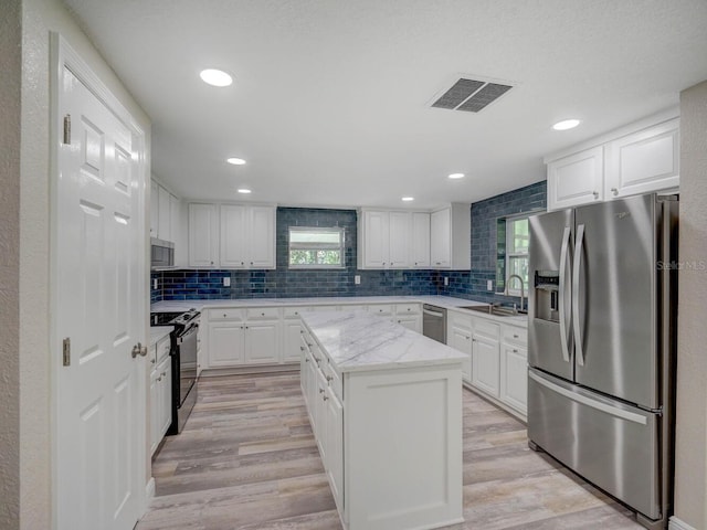 kitchen with visible vents, a sink, a center island, stainless steel appliances, and light wood-style floors