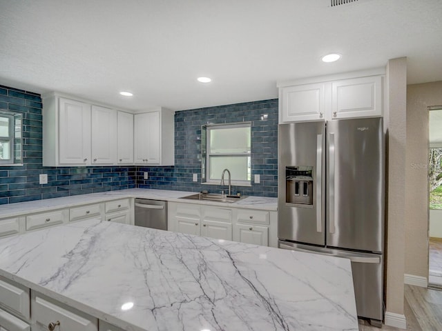 kitchen with tasteful backsplash, light stone countertops, appliances with stainless steel finishes, white cabinetry, and a sink