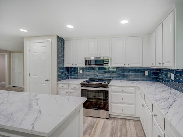 kitchen with tasteful backsplash, white cabinetry, stainless steel appliances, and light wood-type flooring