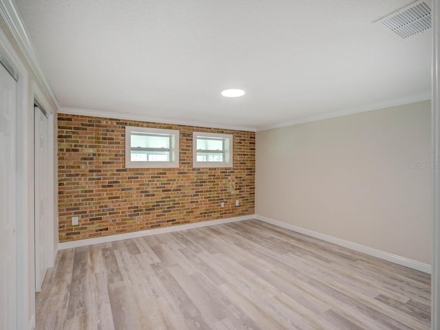 unfurnished room with baseboards, light wood finished floors, visible vents, brick wall, and ornamental molding