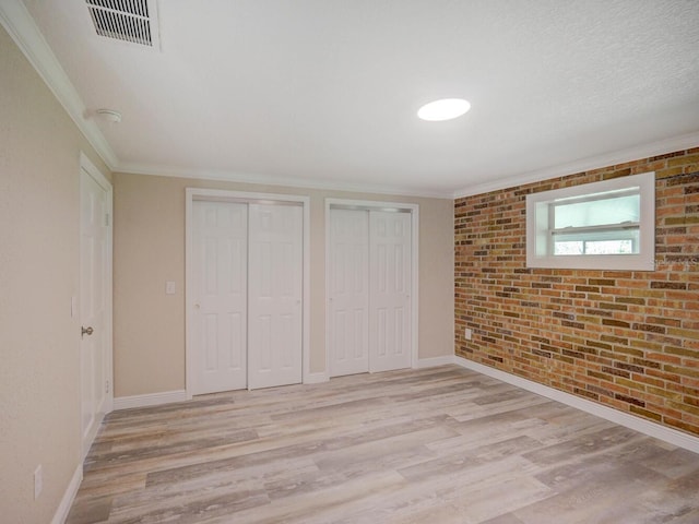 unfurnished bedroom featuring light wood-type flooring, visible vents, multiple closets, and brick wall