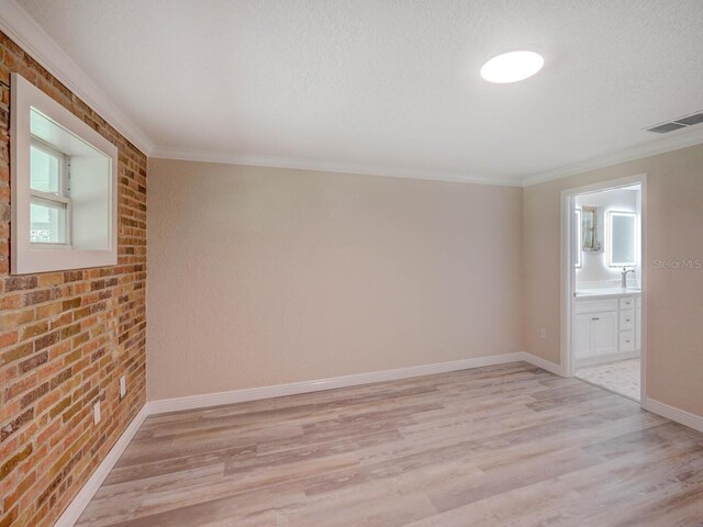 unfurnished room with baseboards, visible vents, brick wall, light wood-style flooring, and ornamental molding