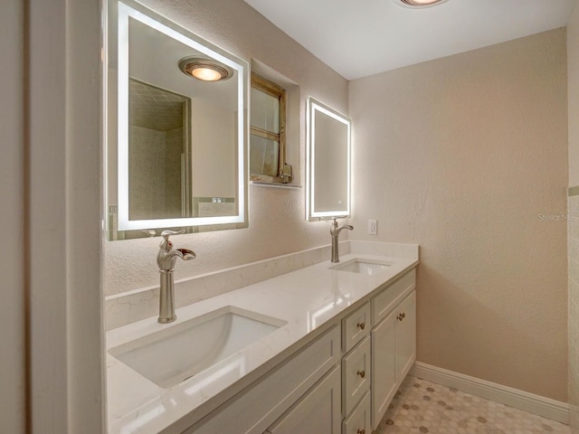 full bath with double vanity, a textured wall, baseboards, and a sink