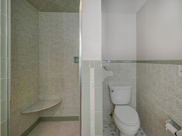 bathroom featuring a wainscoted wall, toilet, and tile walls